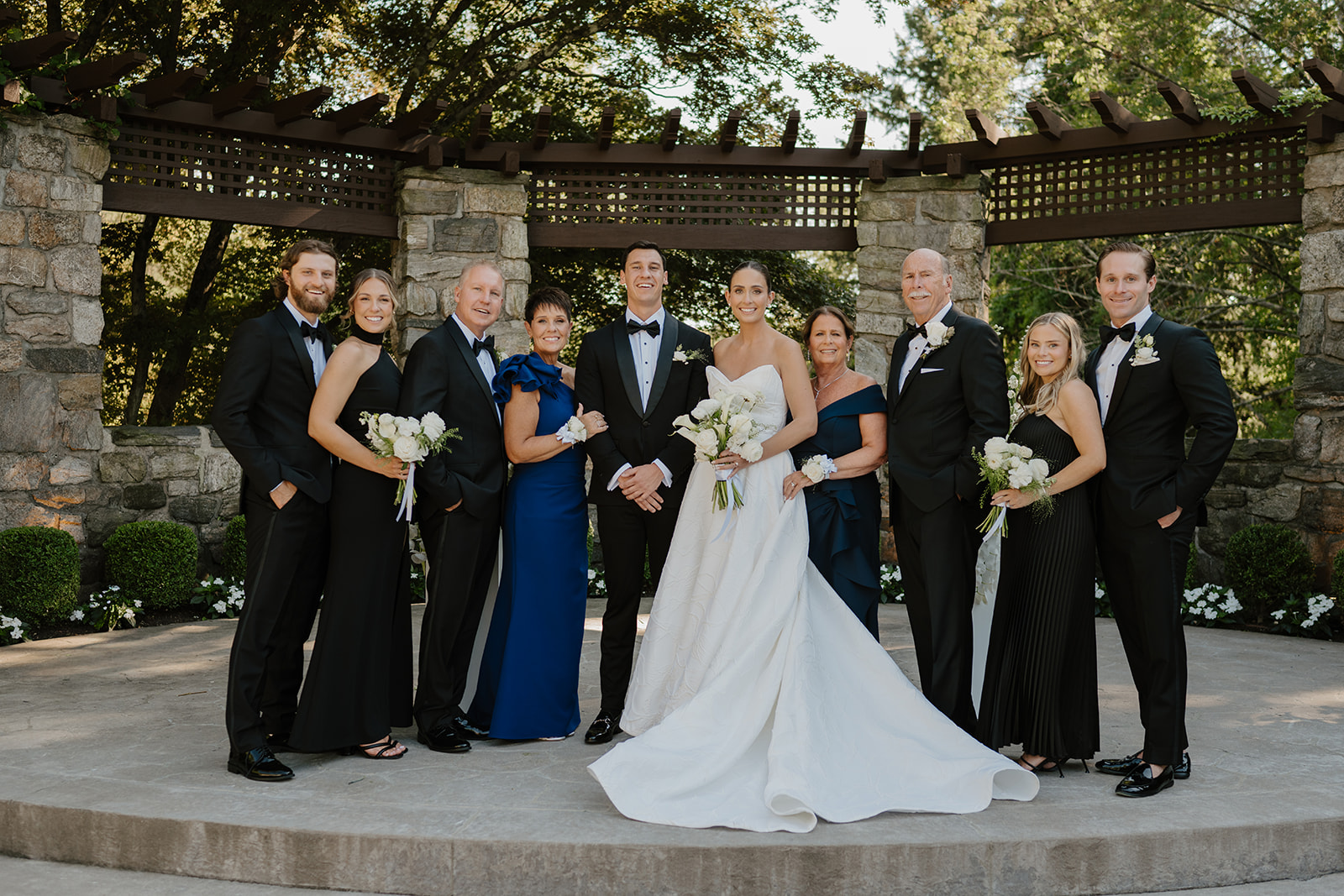 Bride and groom posing for a formal group portrait with their families under a wooden arbor.